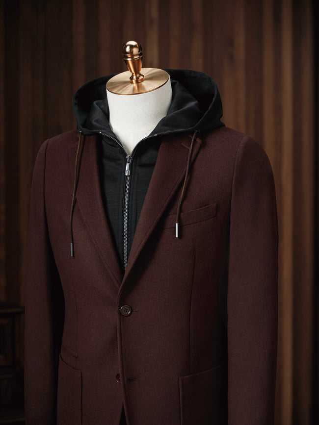 Close-up of men's burgundy blazer with single-button closure, layered over a black zip-up hoodie. Ideal for a sophisticated, casual look blending comfort and style. Perfect for eco-conscious individuals who value high-end, sustainable fashion.