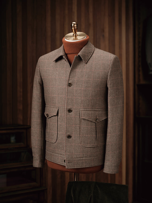 Close-up of a tailored houndstooth field jacket on a mannequin, showcasing fine detailing, sustainable fabric, and classic pockets, ideal for formal wear.