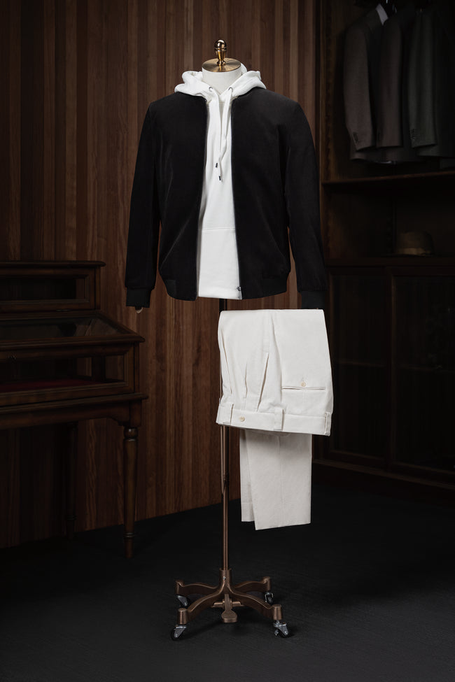 Stylish casual outfit featuring a black tailored zip-up jacket layered over a white hoodie and paired with cream-coloured trousers, displayed on a mannequin for modern streetwear style.