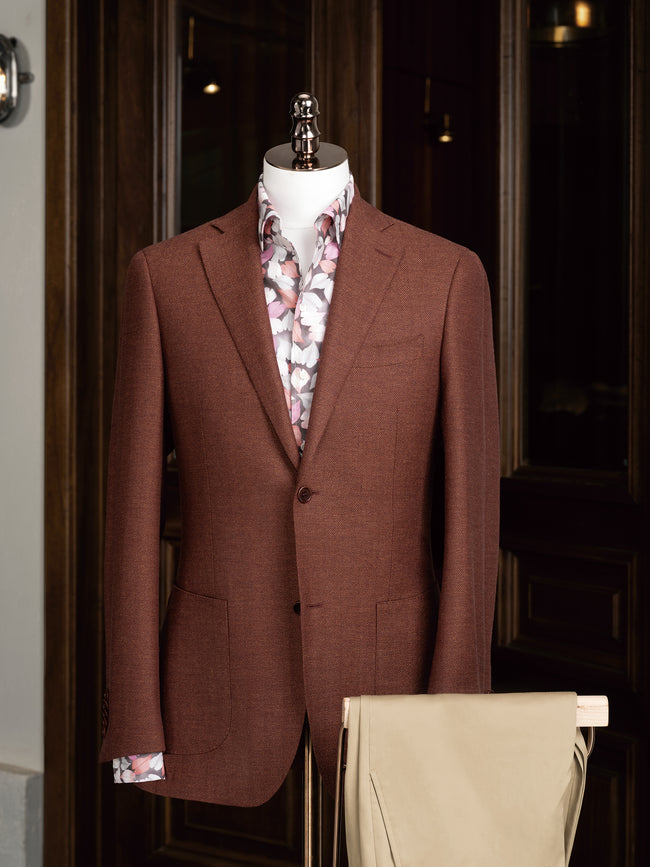 Full outfit on mannequin featuring a rust herringbone blazer and floral button-up shirt, paired with relaxed beige tailored trousers – an effortlessly elegant ensemble for modern suiting.