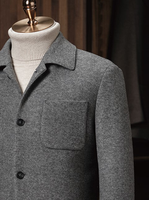 Close-up of a soft grey wool blend jacket with button closure, layered over a cream rollneck knit — combining smart tailoring with relaxed structure.