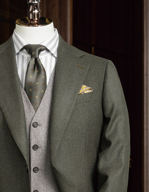 Mannequin dressed in an olive green blazer with a yellow paisley pocket square, grey waistcoat, green tie, and striped shirt – styled for a sophisticated, elegant statement.