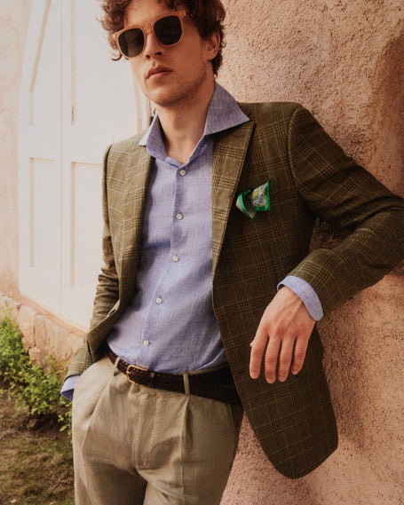 Model Wearing Brown Tailored Jacket with a Blue Undershirt and Beige trousers, Facing the camera leaning on a wall