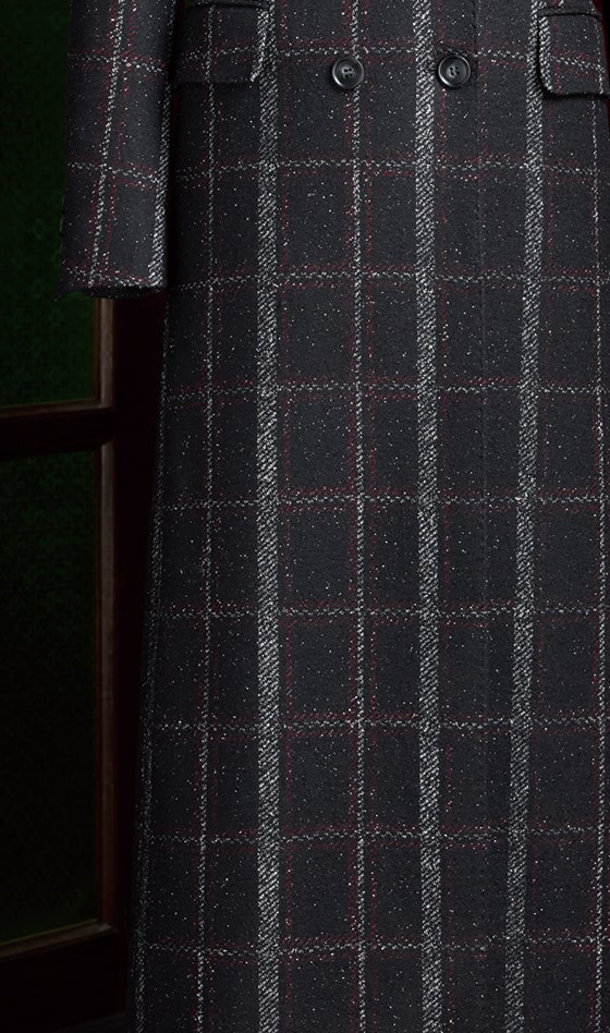 Close-up of bottom half of black plaid overcoat with red and white check pattern, showcasing double-breasted buttons and premium tailored finish.