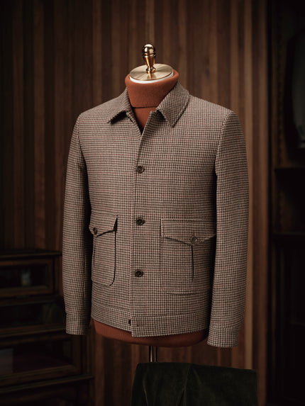 Close-up of a tailored houndstooth field jacket on a mannequin, showcasing fine detailing, sustainable fabric, and classic pockets, ideal for formal wear.