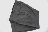 Premium charcoal grey wool trousers by POLLHEIM featuring side adjusters, pleated design, and welt pockets, photographed flat lay against white background