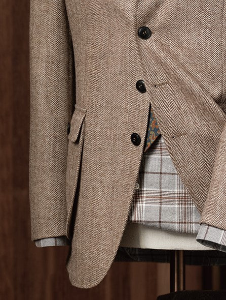 Elegant beige men's tweed blazer on a mannequin with a plaid shirt, floral tie, and pocket square, close up on buttons and pocket