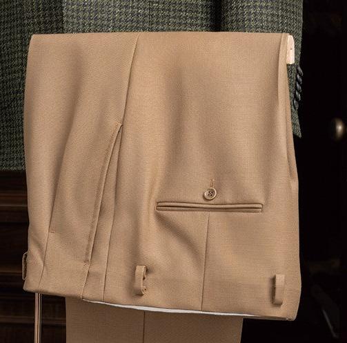 Close-up of beige tailored trousers, featuring a classic design with adjustable side tabs and a sleek pocket detail, paired with a green checked jacket.