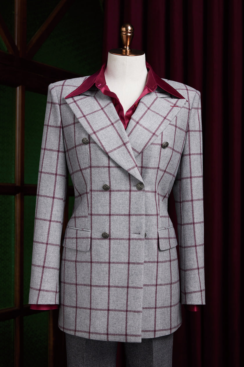 Full mannequin outfit displaying a light grey red check women's suit jacket paired with a maroon shirt and grey trousers, set against dark red drapes and green wall panels.