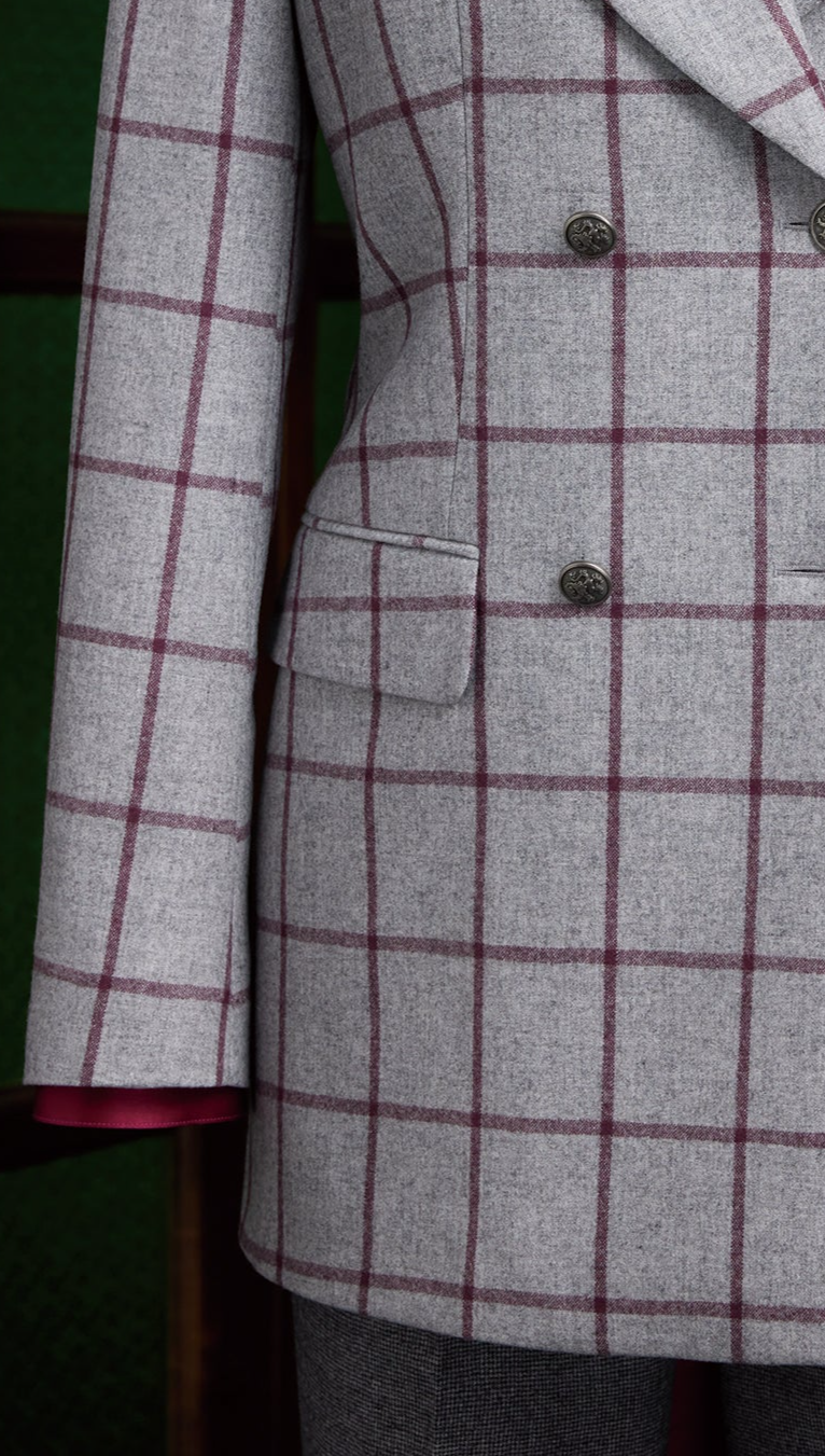 Close-up view of a light grey women's double-breasted blazer with red windowpane check pattern, flap pocket detail and tailored waist.
