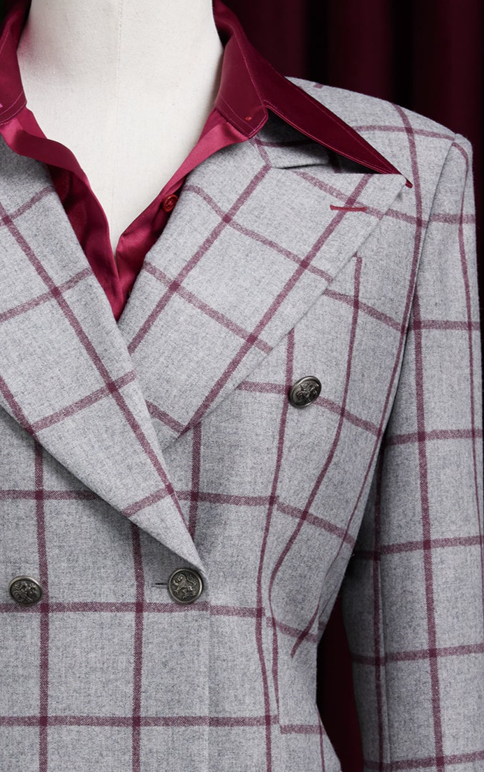 Detailed shot of a tailored light grey blazer with red check and wide peak lapels, styled with a rich maroon satin shirt.