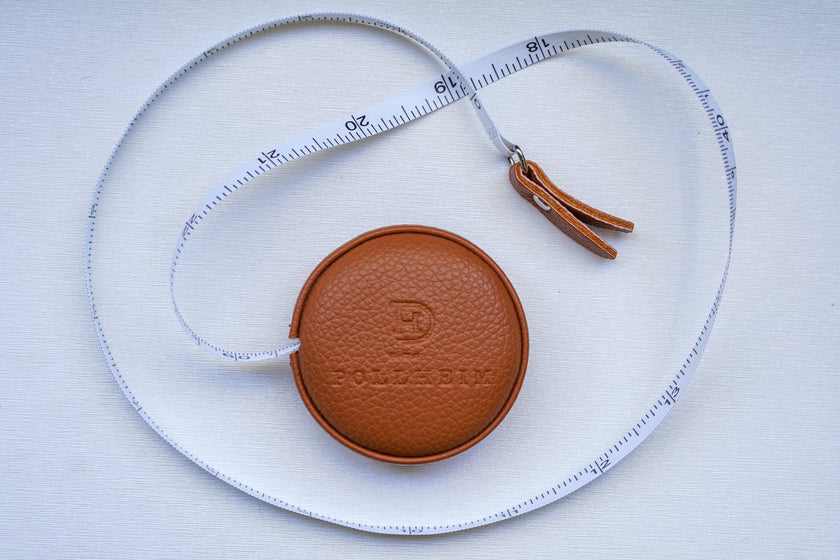 POLLHEIM brown leather retractable tape measure partially extended, elegantly displayed on a light surface – a premium tool for high-end tailoring and garment measurements.
