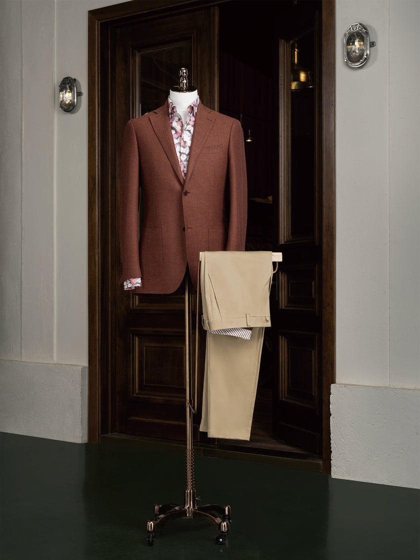 Styled display of a rust-coloured blazer and beige trousers at the entrance of a tailoring studio. The mannequin showcases a patterned floral shirt beneath, ideal for seasonal style or business casual dressing.