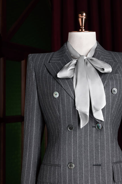 Detailed image of a tailored grey pinstripe suit jacket for women with structured shoulders and satin blouse accent.