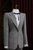 Women's tailored houndstooth suit on mannequin, featuring structured shoulders, fitted waist, and white blouse with black ribbon, exuding vintage elegance.