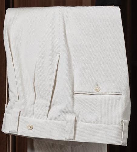 Close-up of cream-colored tailored trousers with cuffed hems and button details, showcasing refined craftsmanship and classic style