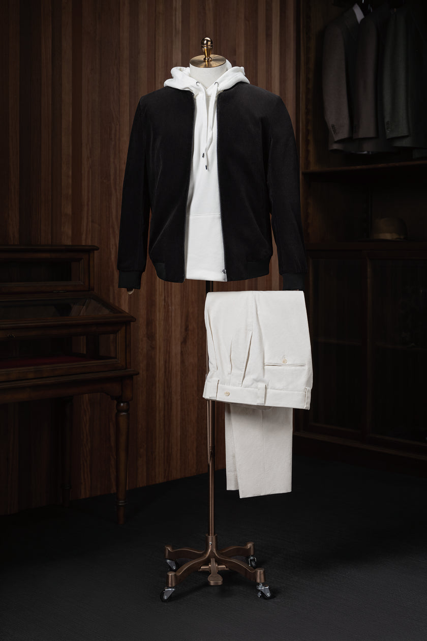 Stylish casual outfit featuring a black tailored zip-up jacket layered over a white hoodie and paired with cream-coloured trousers, displayed on a mannequin for modern streetwear style.