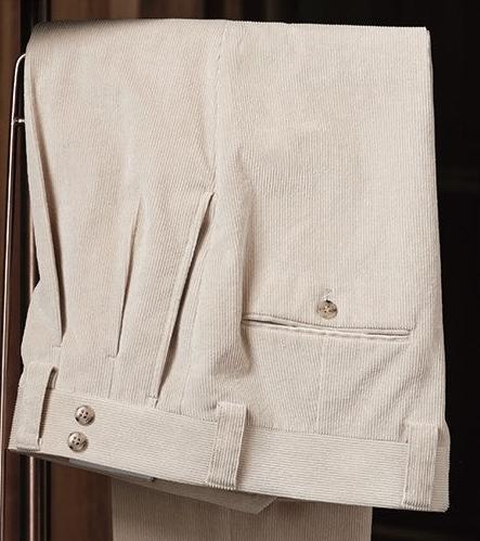 Pleated cream corduroy trousers featuring double side adjusters, buttoned back pocket, and turn-up cuffs — an elevated staple for seasonal menswear dressing.