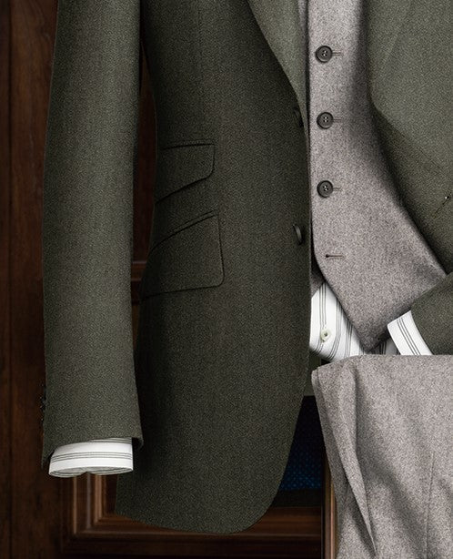 Close-up of an olive green tailored blazer layered over a soft grey waistcoat, paired with a green-striped shirt – showcasing refined layering and bespoke styling.