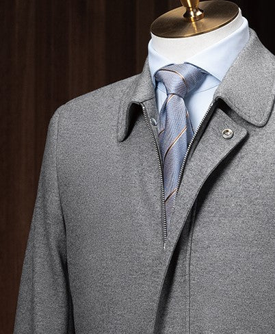 Upper body shot of a grey wool jacket with a zip and snap front closure, paired with a pale blue dress shirt and striped tie — modern layering meets business-casual polish.