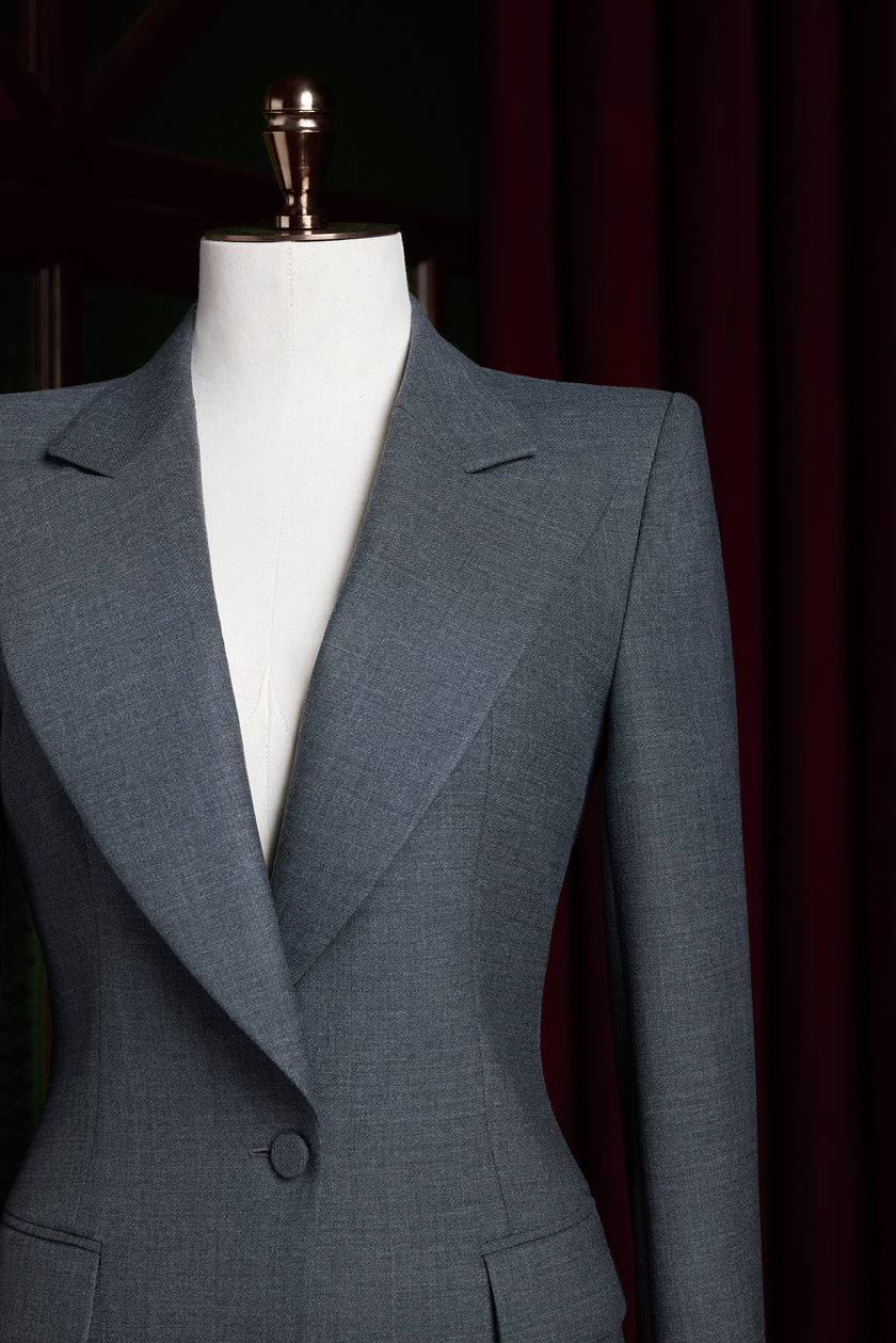 Close-up of a women's tailored grey blazer showing refined notch lapels and structured darting at the waist, highlighting clean craftsmanship.