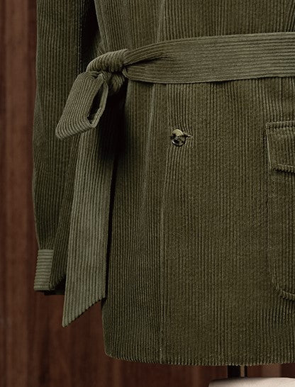 Detail shot of an olive green corduroy belted jacket with side-tie waist and horn button, highlighting relaxed structure and utilitarian design in fine tailoring.