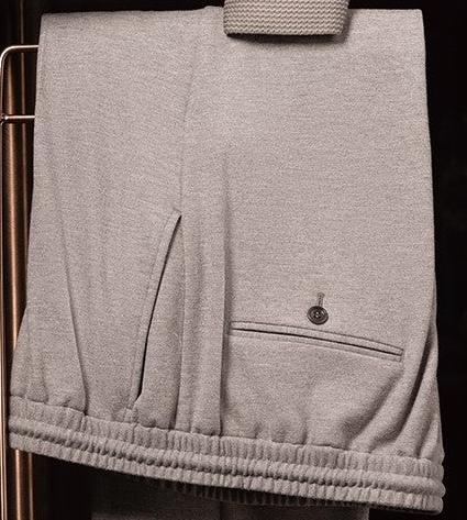 Close-up of stone grey elastic waist trousers with rear buttoned welt pocket and clean side seam, tailored from textured knit fabric for modern comfort and structure.