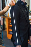 Tailor performing a full sleeve length measurement from shoulder to wrist on a client wearing a black blazer, showcasing the professional use of a POLLHEIM tape measure for made-to-measure accuracy.