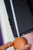Tailor measuring the sleeve length of a bespoke black suit jacket using a POLLHEIM retractable tape measure, focusing on precision tailoring and custom garment adjustments.