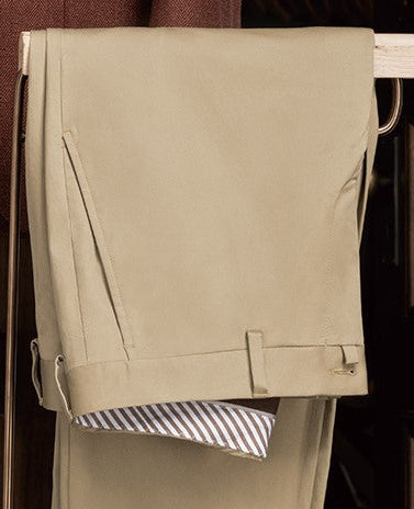 Folded view of bespoke beige trousers featuring a subtle waistband tab extension and visible striped pocket lining, exemplifying classic tailoring and refined craftsmanship.